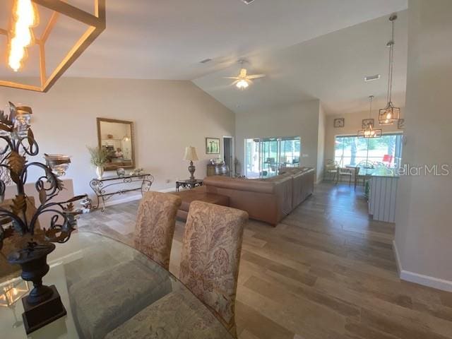 dining area with hardwood / wood-style flooring, ceiling fan with notable chandelier, and vaulted ceiling