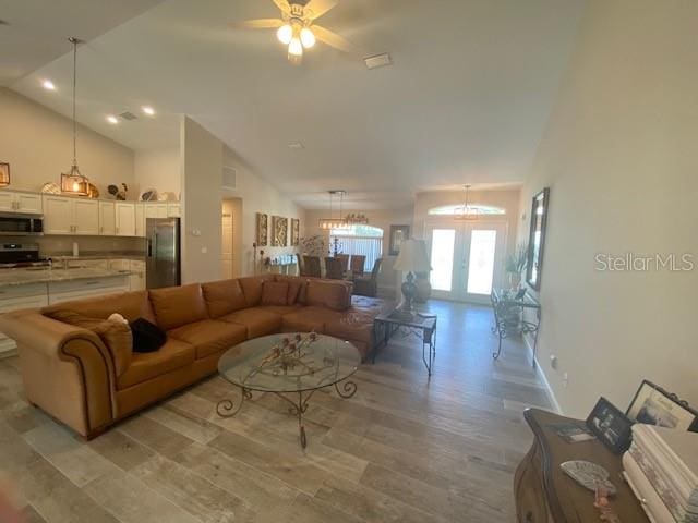 living room featuring french doors, vaulted ceiling, ceiling fan with notable chandelier, and light hardwood / wood-style floors