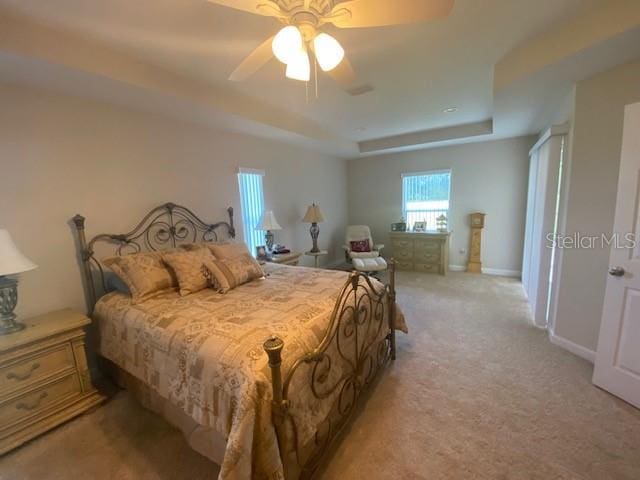 carpeted bedroom with a tray ceiling and ceiling fan