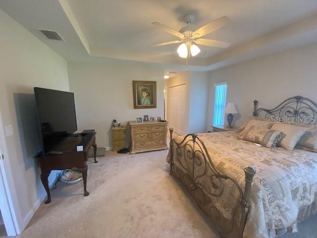 bedroom with a raised ceiling, light colored carpet, a closet, and ceiling fan