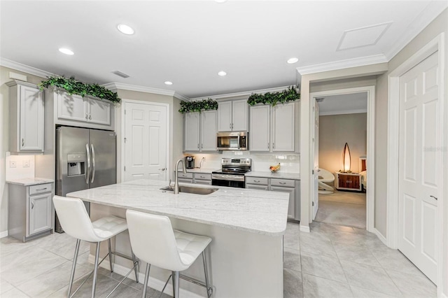 kitchen with appliances with stainless steel finishes, light stone counters, gray cabinetry, a kitchen island with sink, and sink