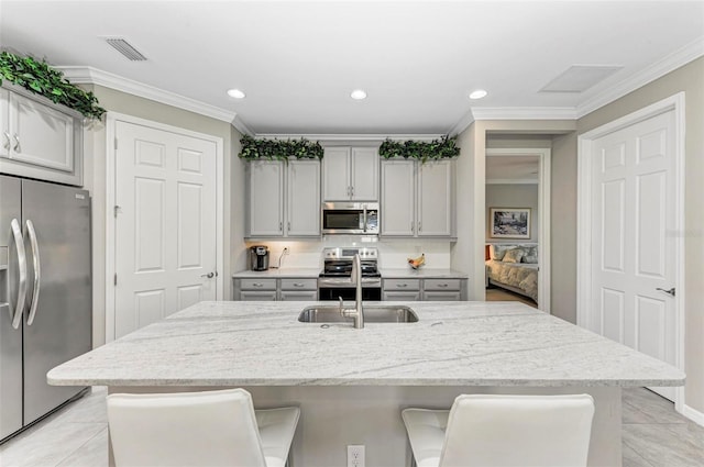 kitchen featuring light stone countertops, sink, a kitchen breakfast bar, gray cabinets, and appliances with stainless steel finishes