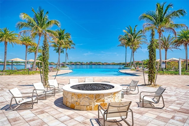 view of pool featuring a water view, an outdoor fire pit, and a patio area