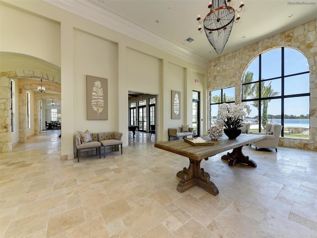 interior space featuring a high ceiling, a water view, crown molding, and a notable chandelier