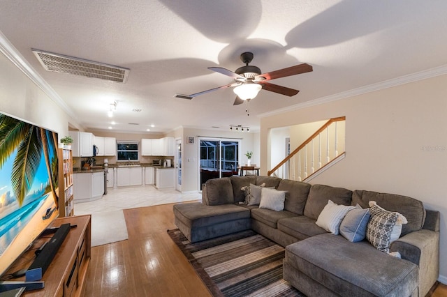 living room with light hardwood / wood-style floors, ornamental molding, a textured ceiling, and ceiling fan