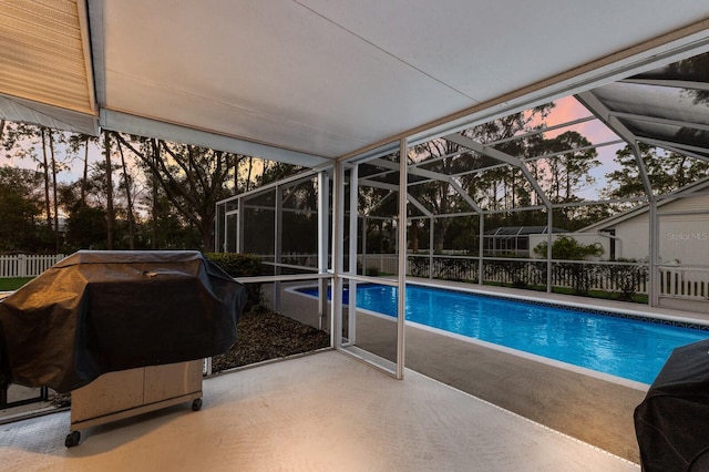 pool at dusk featuring a patio, grilling area, and glass enclosure