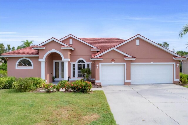 7341 Featherstone Blvd, Sarasota, FL 34238 - mediterranean / spanish-style house featuring an attached garage, a tiled roof, a front lawn, and stucco siding