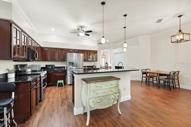 kitchen with an island with sink, dark brown cabinets, hanging light fixtures, stainless steel appliances, and dark wood-type flooring