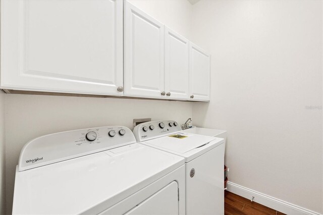 clothes washing area featuring sink, dark wood-type flooring, washing machine and clothes dryer, and cabinets