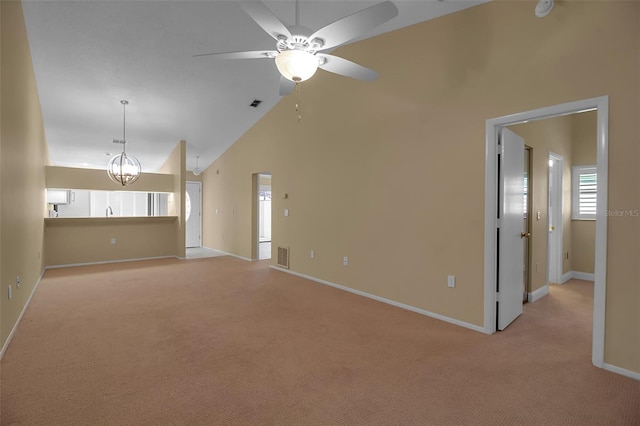 unfurnished living room with ceiling fan with notable chandelier, light colored carpet, and high vaulted ceiling