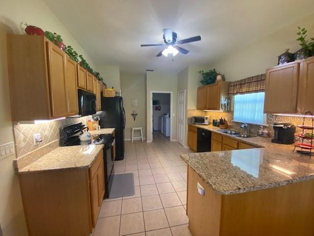 kitchen with kitchen peninsula, light tile patterned floors, light stone countertops, black appliances, and sink