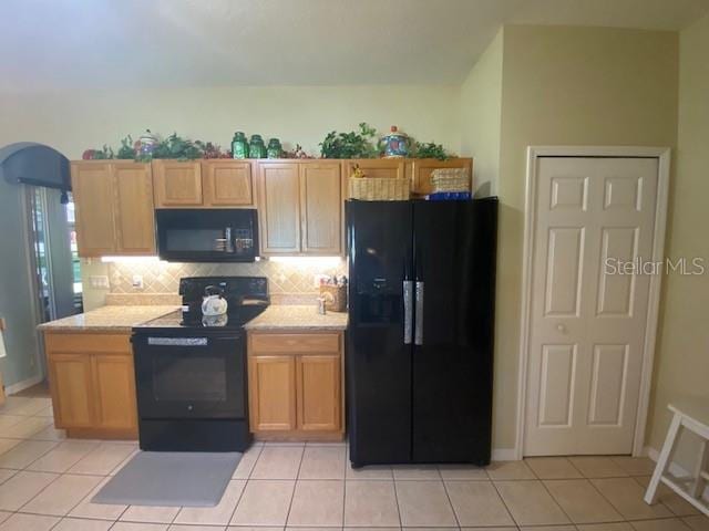 kitchen with black appliances, light stone counters, backsplash, and light tile patterned floors