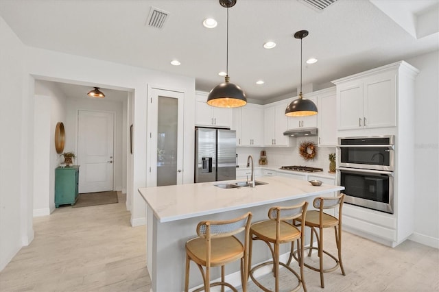 kitchen featuring white cabinets, appliances with stainless steel finishes, a kitchen island with sink, pendant lighting, and sink