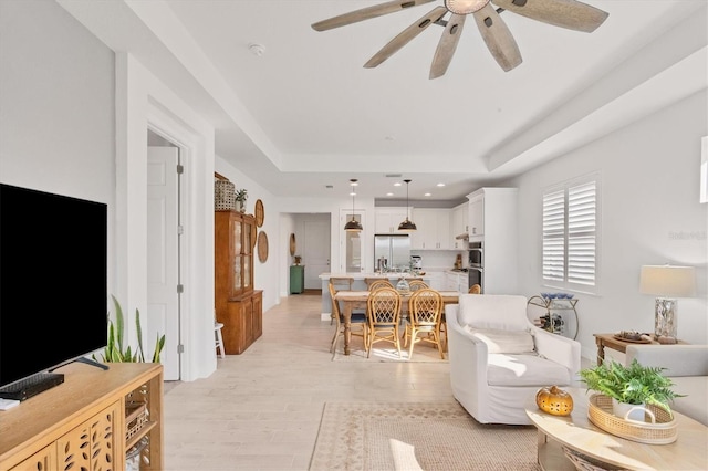 living room featuring ceiling fan, light wood-type flooring, and a raised ceiling