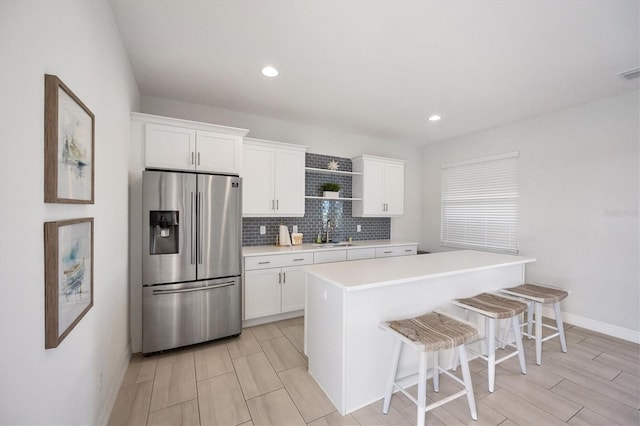 kitchen featuring sink, a kitchen bar, a center island, white cabinetry, and stainless steel fridge with ice dispenser