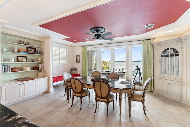 dining area featuring french doors, a tray ceiling, ceiling fan, a water view, and crown molding