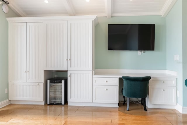 office area with built in desk, beamed ceiling, wooden ceiling, wine cooler, and light hardwood / wood-style flooring