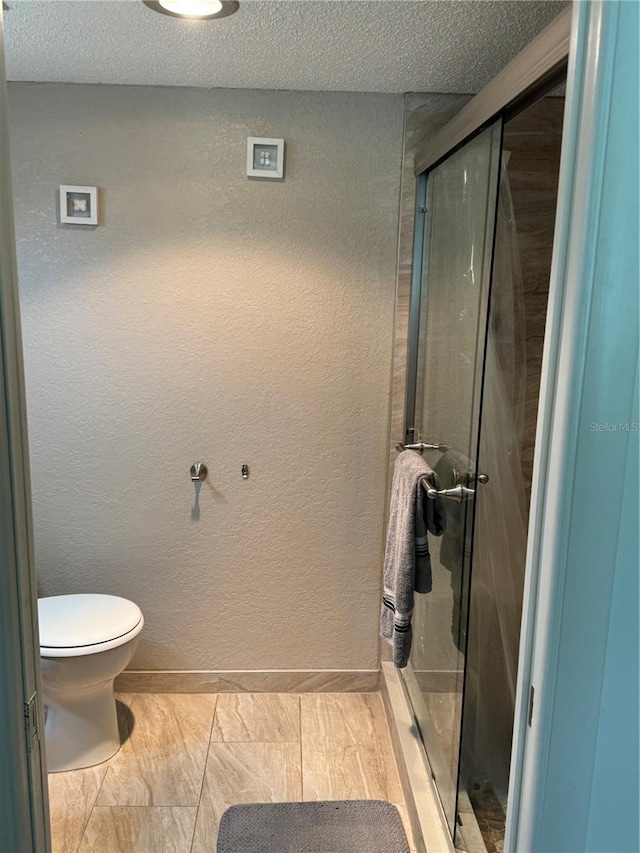 bathroom featuring a shower with door, toilet, and a textured ceiling