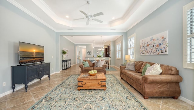 tiled living room featuring ornamental molding, a tray ceiling, and ceiling fan with notable chandelier