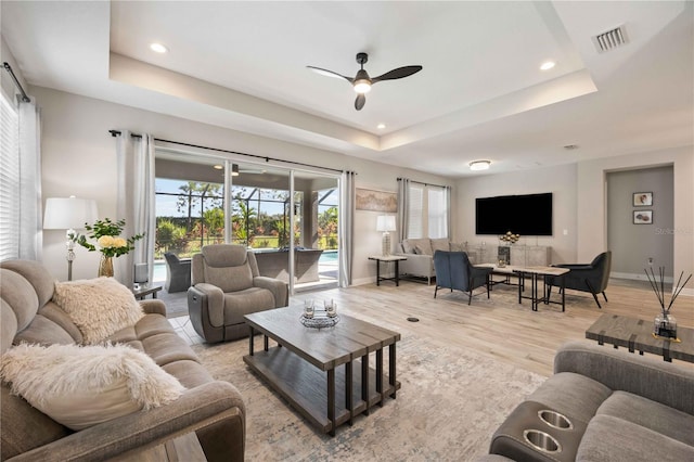 living room with light hardwood / wood-style flooring, ceiling fan, and a raised ceiling