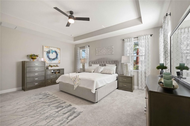 bedroom featuring light carpet, a tray ceiling, and ceiling fan