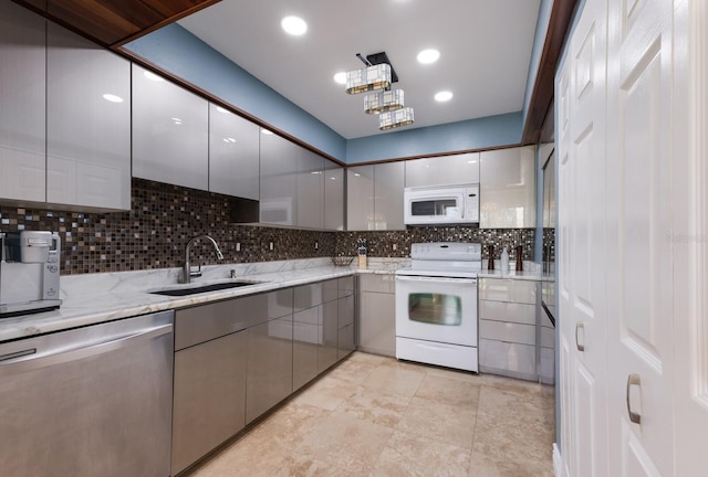 kitchen with gray cabinetry, white appliances, backsplash, sink, and light stone counters