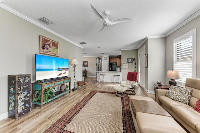 living room with ornamental molding, a textured ceiling, light wood-type flooring, and ceiling fan