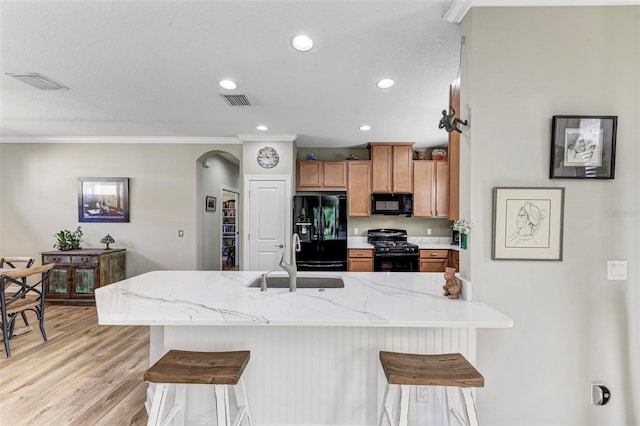 kitchen with sink, black appliances, light hardwood / wood-style flooring, and a kitchen breakfast bar