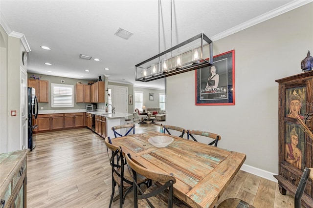 dining space with light hardwood / wood-style flooring, ornamental molding, a healthy amount of sunlight, and sink