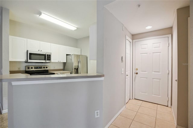 kitchen featuring kitchen peninsula, stainless steel appliances, white cabinets, decorative backsplash, and light tile patterned floors