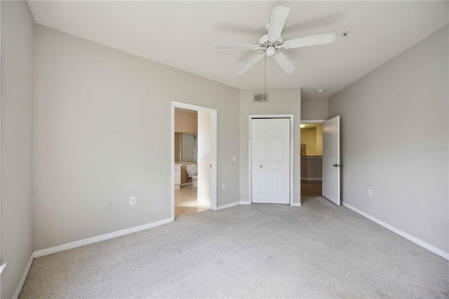 unfurnished bedroom featuring a closet, ensuite bathroom, light colored carpet, and ceiling fan