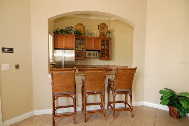 kitchen featuring sink, stainless steel fridge, a kitchen bar, crown molding, and light tile patterned floors