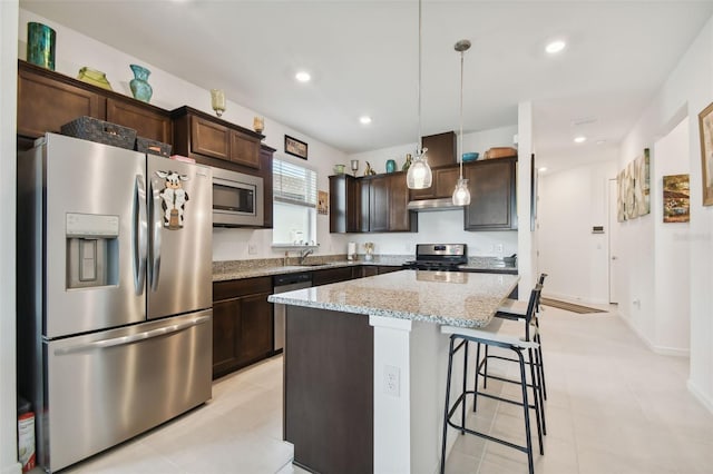 kitchen featuring light stone countertops, a kitchen island, stainless steel appliances, dark brown cabinetry, and pendant lighting