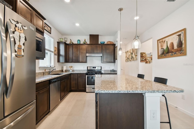 kitchen featuring a kitchen island, a breakfast bar, dark brown cabinetry, decorative light fixtures, and appliances with stainless steel finishes