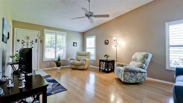 living area with a textured ceiling, ceiling fan, baseboards, light wood finished floors, and vaulted ceiling