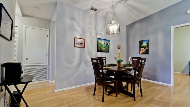 dining area featuring visible vents, light wood-style floors, a notable chandelier, and baseboards