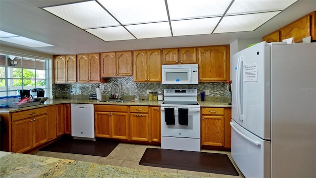 kitchen with brown cabinetry, white appliances, backsplash, and a sink