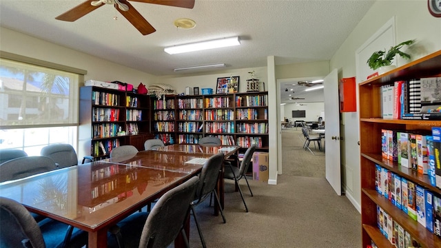 home office featuring a textured ceiling, ceiling fan, bookshelves, and carpet floors