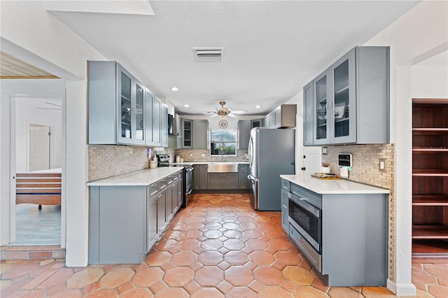 kitchen featuring stainless steel appliances, tasteful backsplash, gray cabinets, ceiling fan, and sink