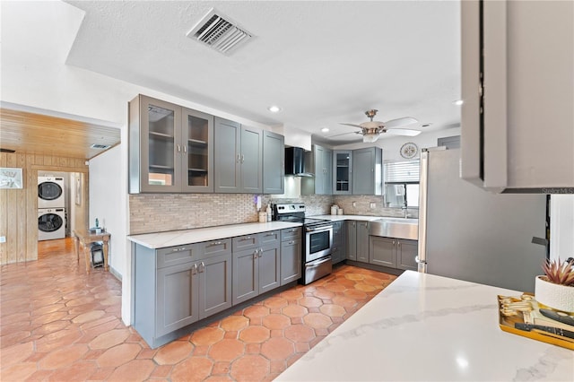 kitchen featuring stainless steel electric range, light stone countertops, ceiling fan, decorative backsplash, and stacked washer and dryer