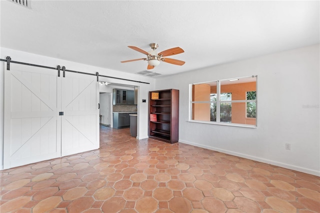 empty room featuring a barn door, visible vents, baseboards, and a ceiling fan
