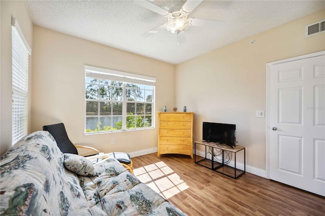 living area with baseboards, a textured ceiling, visible vents, and wood finished floors