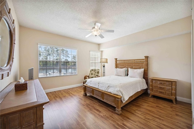 bedroom featuring ceiling fan, a textured ceiling, baseboards, and wood finished floors