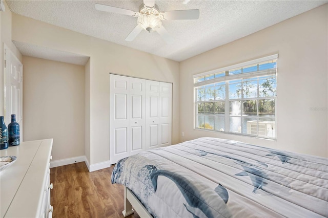 bedroom with a textured ceiling, a closet, wood finished floors, and baseboards