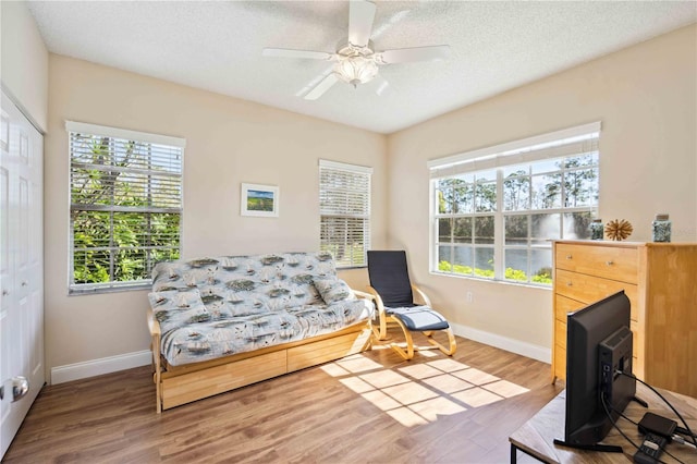 living area with ceiling fan, a textured ceiling, baseboards, and wood finished floors