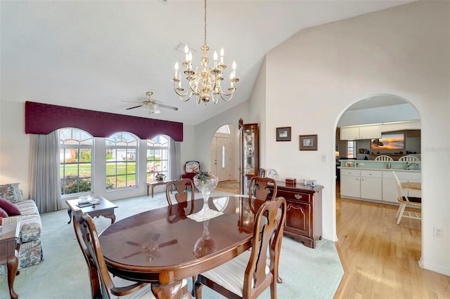 dining space with high vaulted ceiling, ceiling fan with notable chandelier, and light hardwood / wood-style floors