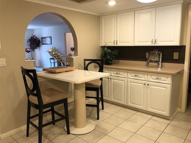 kitchen with white cabinets, light tile patterned floors, a kitchen bar, and decorative backsplash