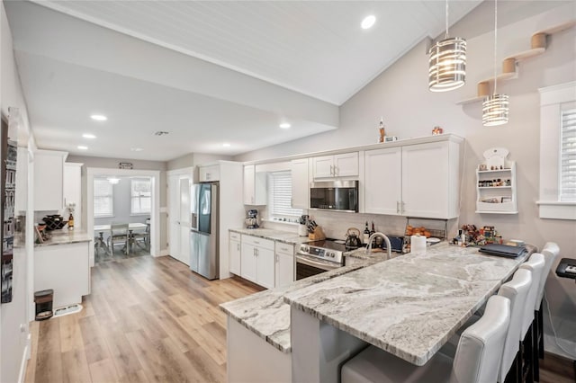 kitchen with kitchen peninsula, appliances with stainless steel finishes, white cabinetry, and lofted ceiling