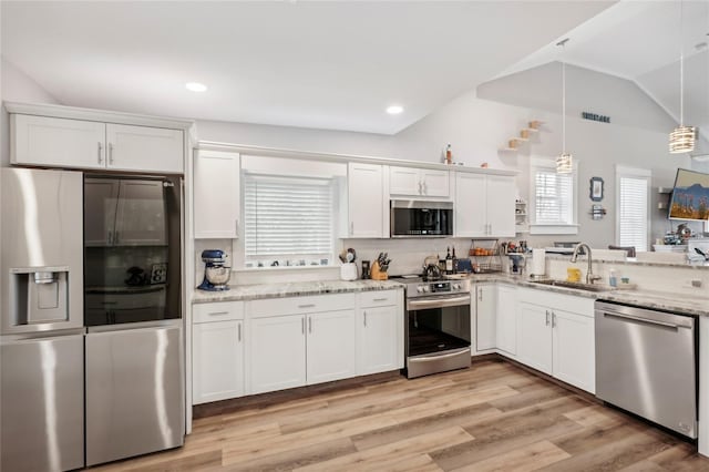 kitchen with pendant lighting, lofted ceiling, white cabinets, sink, and appliances with stainless steel finishes