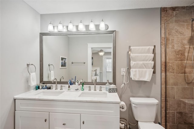 bathroom featuring a tile shower, ceiling fan, vanity, and toilet